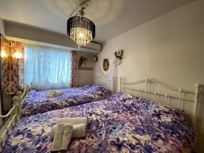 A bedroom with two beds, floral bedspreads, a chandelier, and a window with curtains. - AMS TOWER Nakajima (Sapporo)