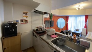 Une petite cuisine équipée d’une machine à café, d’un évier et d’une fenêtre ornée d’un rideau rouge.
