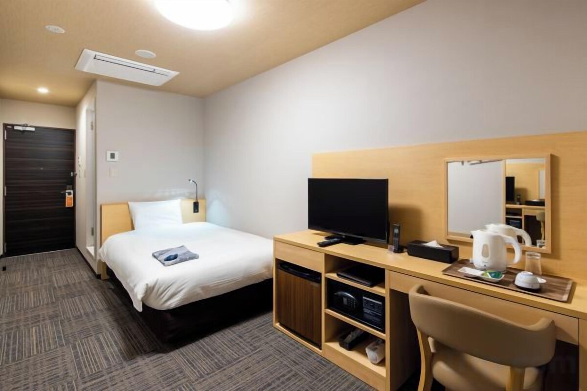 A hotel room with a bed, a desk with a television, a coffee maker, and a mirror.