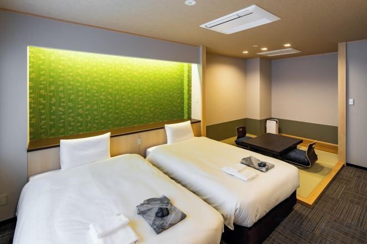 A hotel room with two beds, a small table, a sofa, and a green patterned wall.