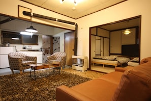 Una sala de estar con un sofá marrón, un sillón estampado y una mesa de centro. Hay un calentador pequeño y un televisor en la esquina.