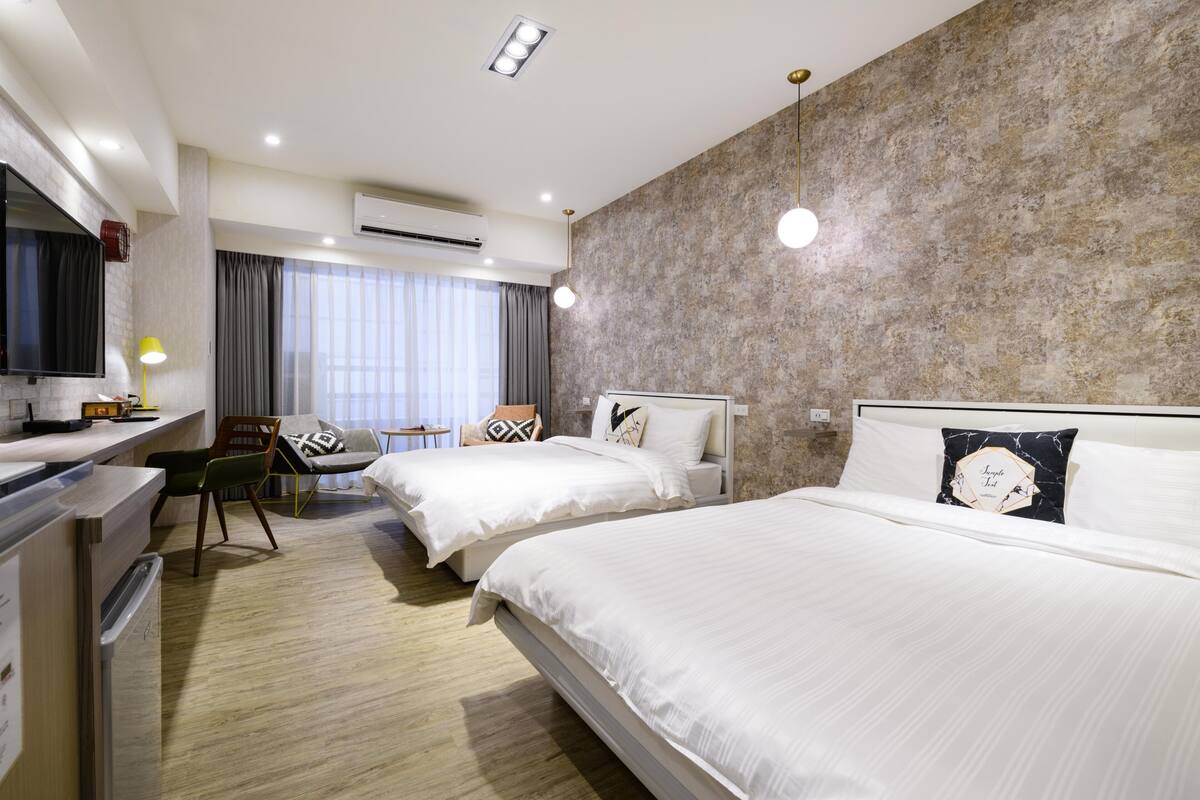 A hotel room with two beds, a desk, a chair, and a TV.