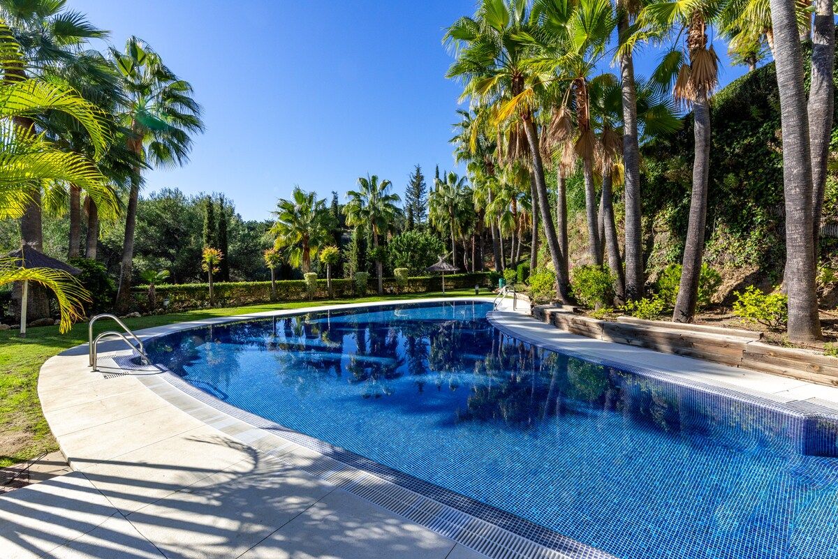 A swimming pool surrounded by palm trees and greenery.