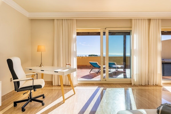 A hotel room with a desk, chair, lamp, and a view of the outdoors through a sliding glass door.