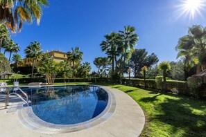 A swimming pool with a clear blue water surface, surrounded by a well-maintained lawn and palm trees.
