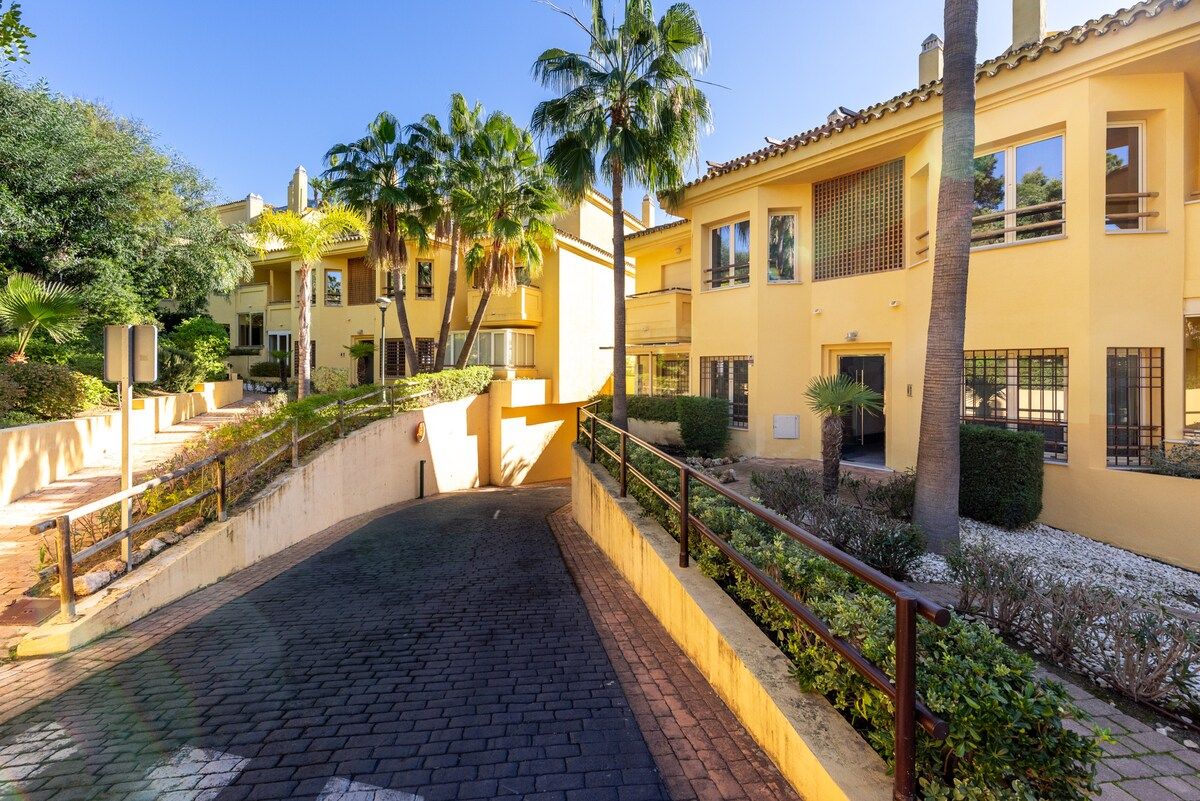 Un patio con un sendero empedrado, palmeras y un edificio amarillo con múltiples ventanas y balcones.