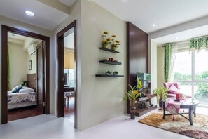 A modern living room with a TV, shelves with plants, a sofa, and a view of greenery outside.