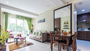 Een moderne woonkamer met een eethoek, een bank, een salontafel en een keuken met donkerhouten kastjes en een grote spiegel.