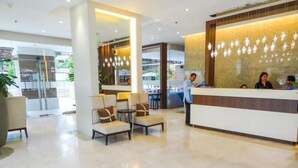 Een moderne hotellobby met een receptiebalie, een zithoek en grote ramen.