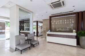 A hotel lobby with a reception desk, seating area, and a large potted plant.
