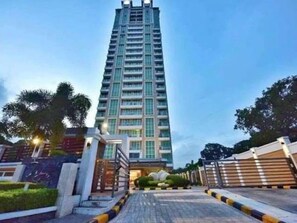 A tall, modern high-rise building with a central entrance and a gated driveway.