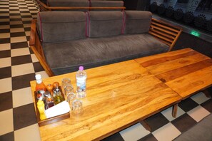 A checkered floor, a wooden table with a bottle of water, and a grey sofa with red piping. - Hotel Las Vegas (Jaipur)