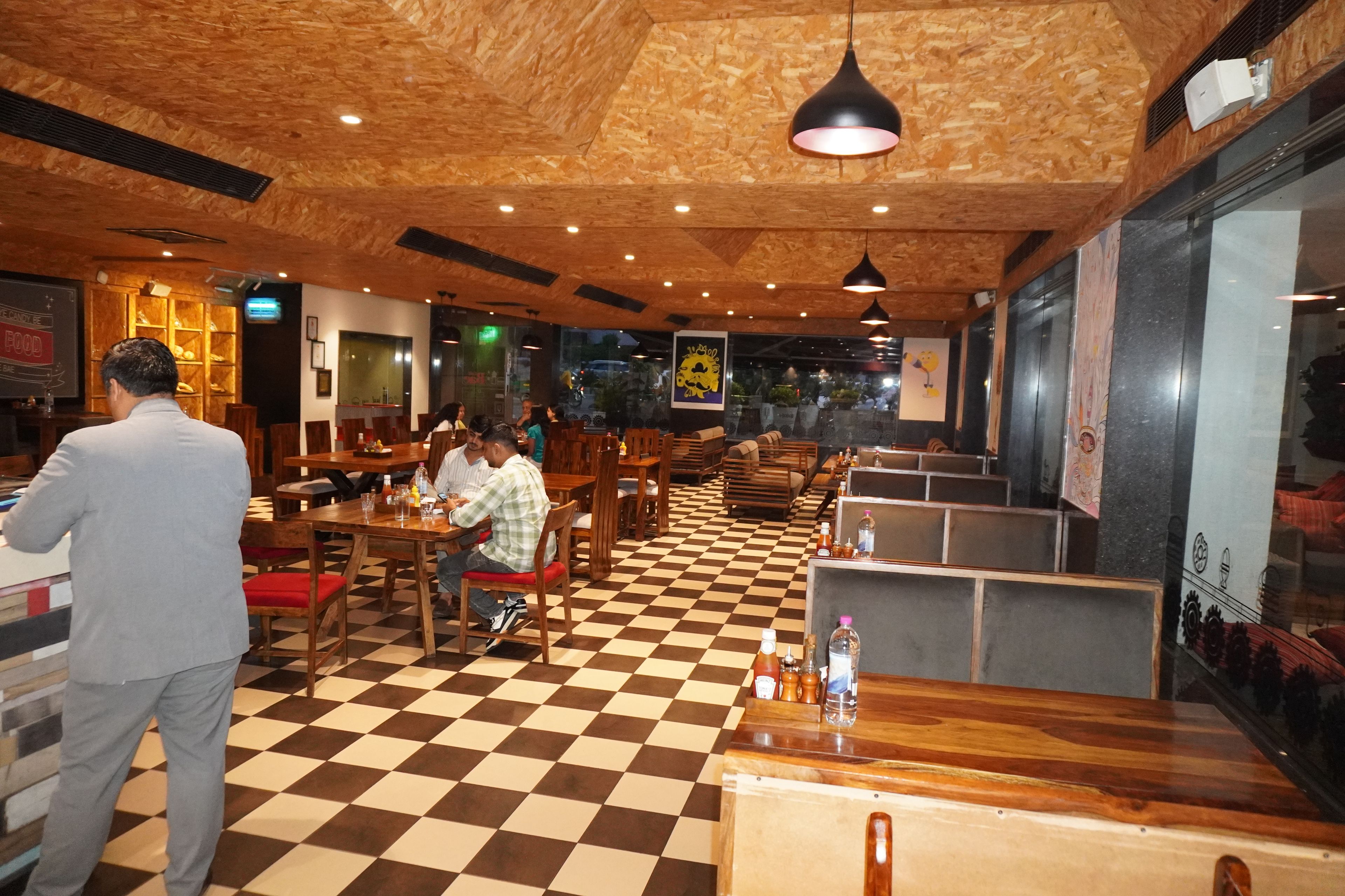 Un interior de restaurante con suelo de madera, varias áreas de estar y lámparas colgantes.
