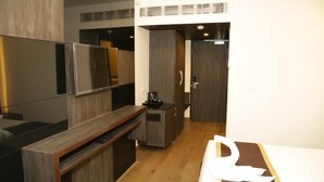 Quarto de hotel moderno com televisão de tela plana, móveis de madeira, minibar e uma porta que dá para outro quarto.