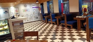 Een café met zwart-witte vloertegels, houten tafels en stoelen, en een vitrine met desserts.