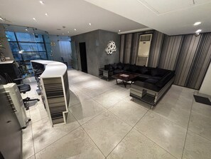 A modern living room with a sofa, coffee table, and a kitchen area with a refrigerator and a microwave. - Hotel Las Vegas (Jaipur)