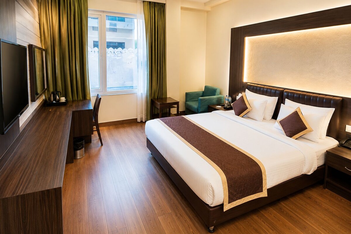 Habitación de hotel con una cama grande, un escritorio, una silla, un televisor y una ventana con cortinas.