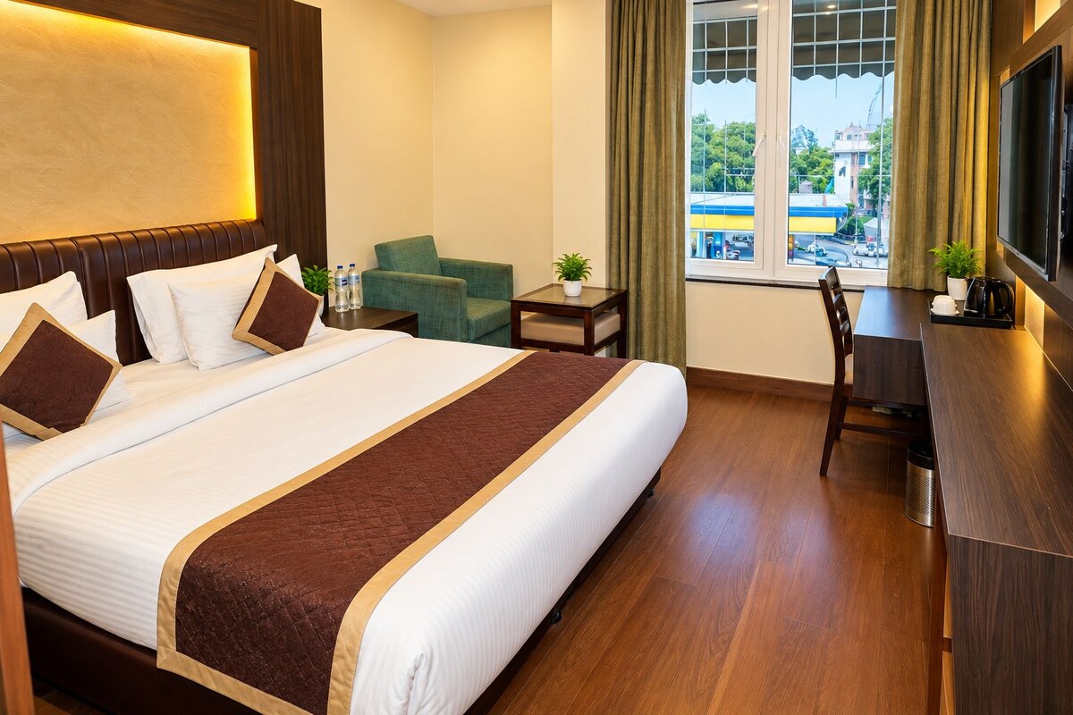 A hotel room with a large bed, a desk, a chair, a small table, and a window with curtains.
