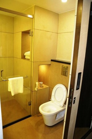 Un baño compacto con cabina de ducha de vidrio, inodoro y un pequeño estante con artículos de aseo.