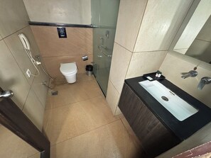 A bathroom with a toilet, a sink, a mirror, and a shower area. - Hotel Las Vegas (Jaipur)