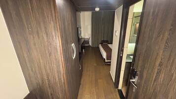 Un pasillo estrecho con suelo de madera que conduce a una habitación con cama y ventana.