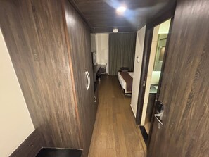 Un pasillo estrecho con suelo de madera que conduce a una habitación con cama y ventana.