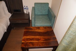 A small hotel room with a bed, a wooden nightstand, a green armchair, and a small table. - Hotel Las Vegas (Jaipur)