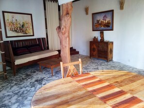 A living room with a wooden dining table, a sofa, a chair, a cabinet, and two paintings on the walls.