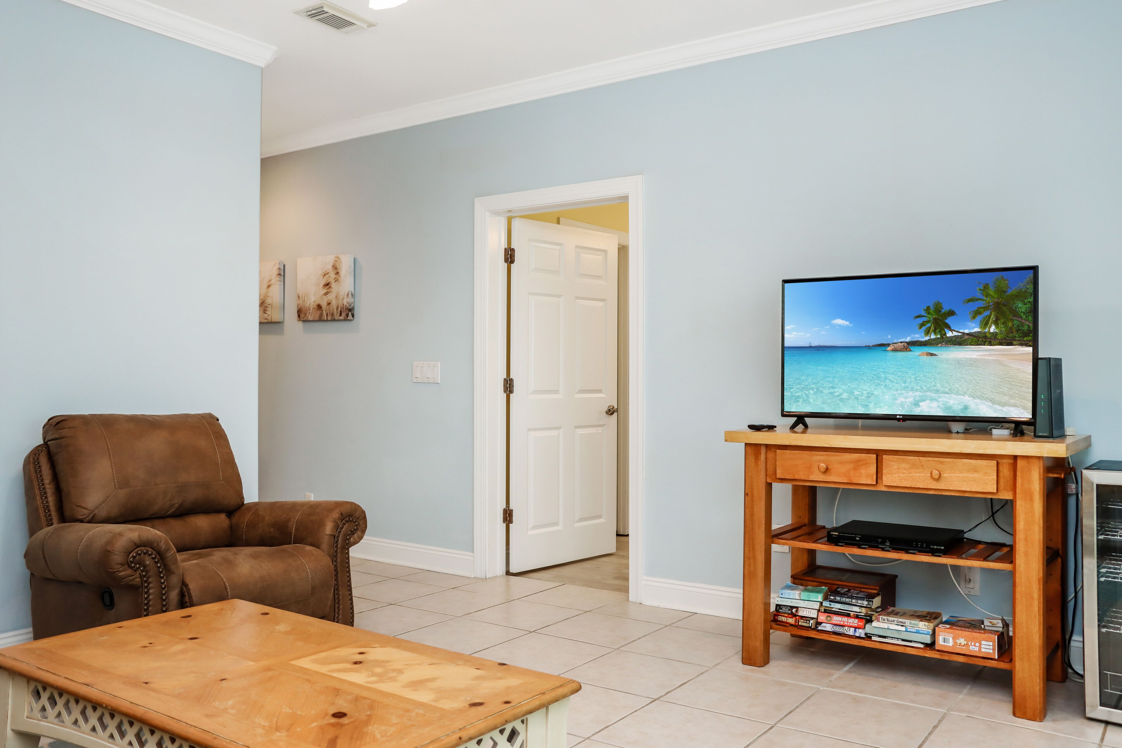 A living room with a brown leather chair, a wooden coffee table, a TV on a wooden stand, and a bookshelf.