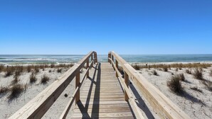 Een houten looppad dat naar het strand leidt, onder heldere luchten.