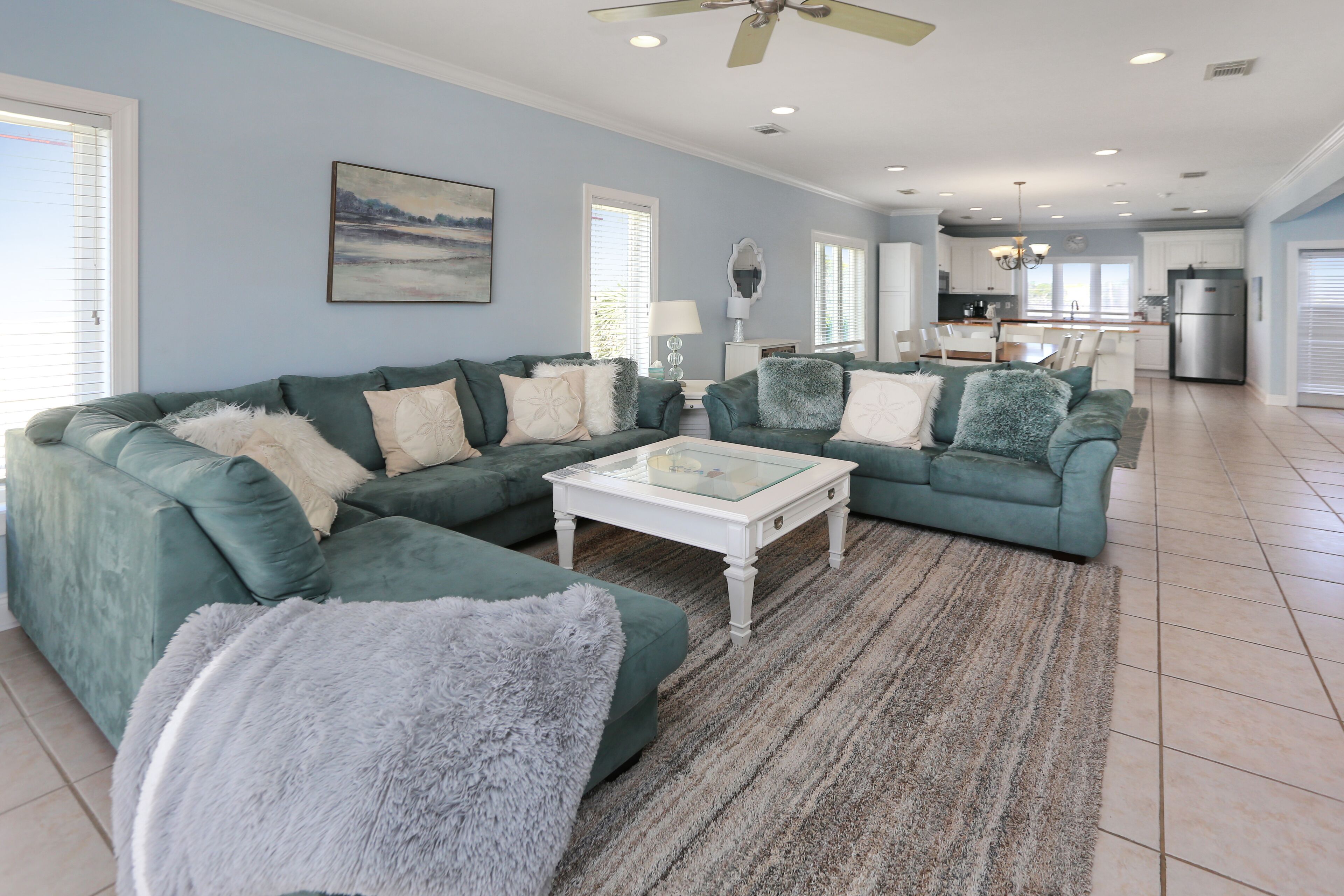 A spacious living room with teal sofas, a white coffee table, and a large window.