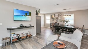A modern living room with a flat-screen TV, a dining area with a table and chairs, and a kitchen area with a refrigerator. - Single Level, Close To Beach, Great Beach View Covered Deck ~ Salt Cured (Cape San Blas)