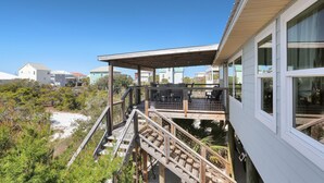 A coastal house with a wooden deck and balcony, surrounded by greenery and other buildings. - Single Level, Close To Beach, Great Beach View Covered Deck ~ Salt Cured (Cape San Blas)
