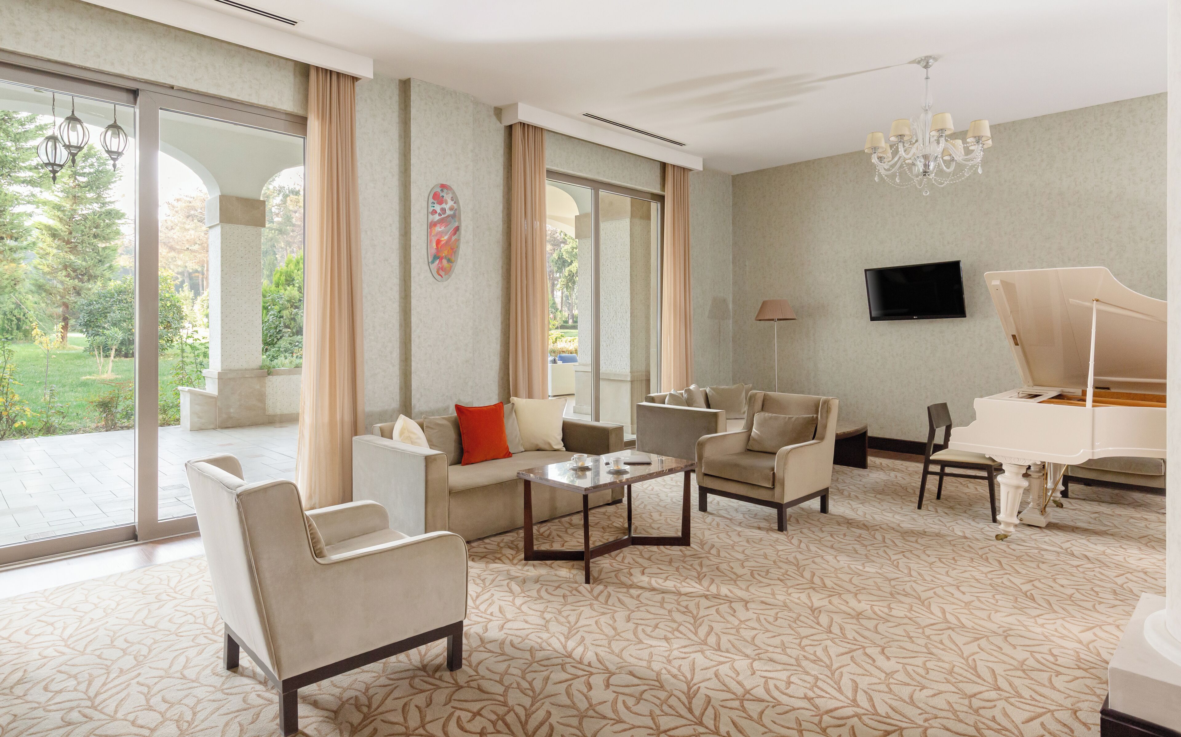 Un salon spacieux comprenant un canapé, des fauteuils, une table basse, un piano et de grandes fenêtres donnant sur l’extérieur.