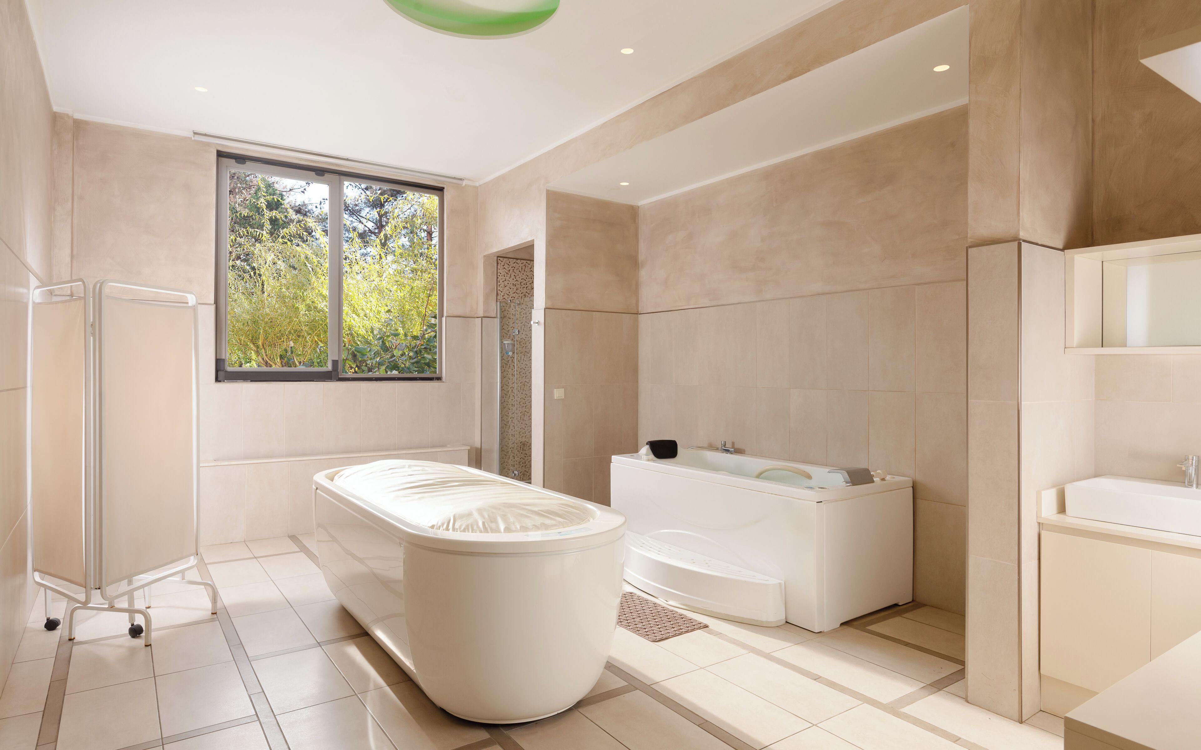 Ein modernes Badezimmer mit einer freistehenden Badewanne, einer Duschkabine und einem großen Fenster für viel Tageslicht.