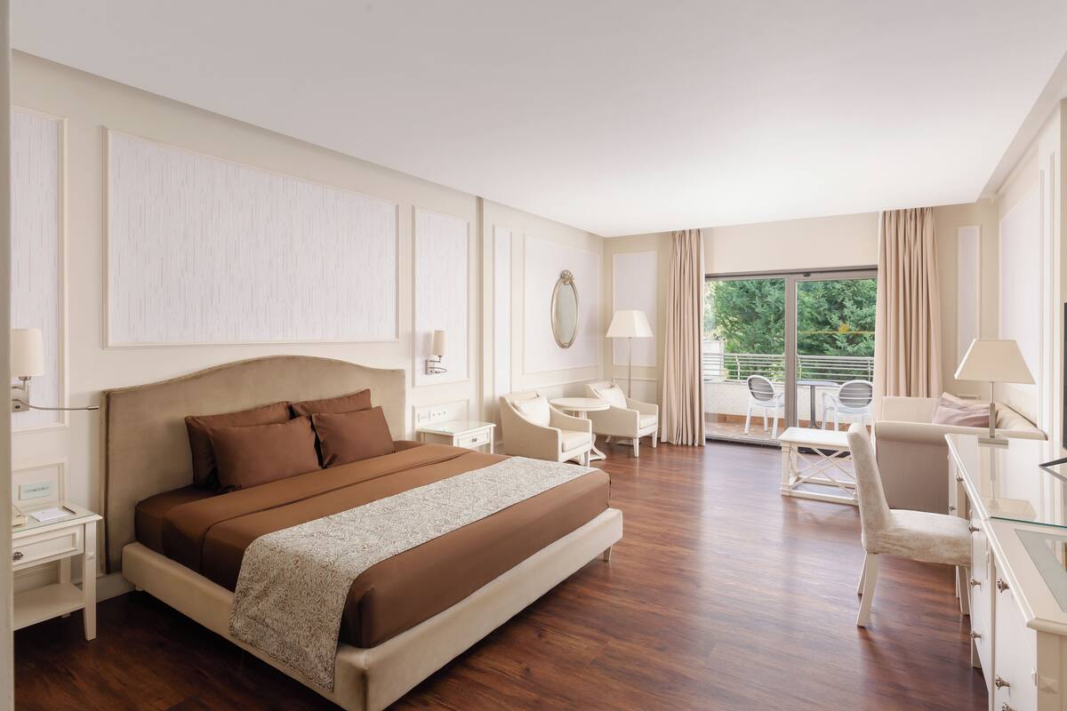 Quarto de hotel com uma cama grande, uma escrivaninha, uma cadeira, televisão e varanda com área de estar externa.
