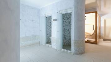 Une salle de bain spacieuse et moderne, dotée d’un grand miroir, d’une zone douche et d’un sol carrelé.