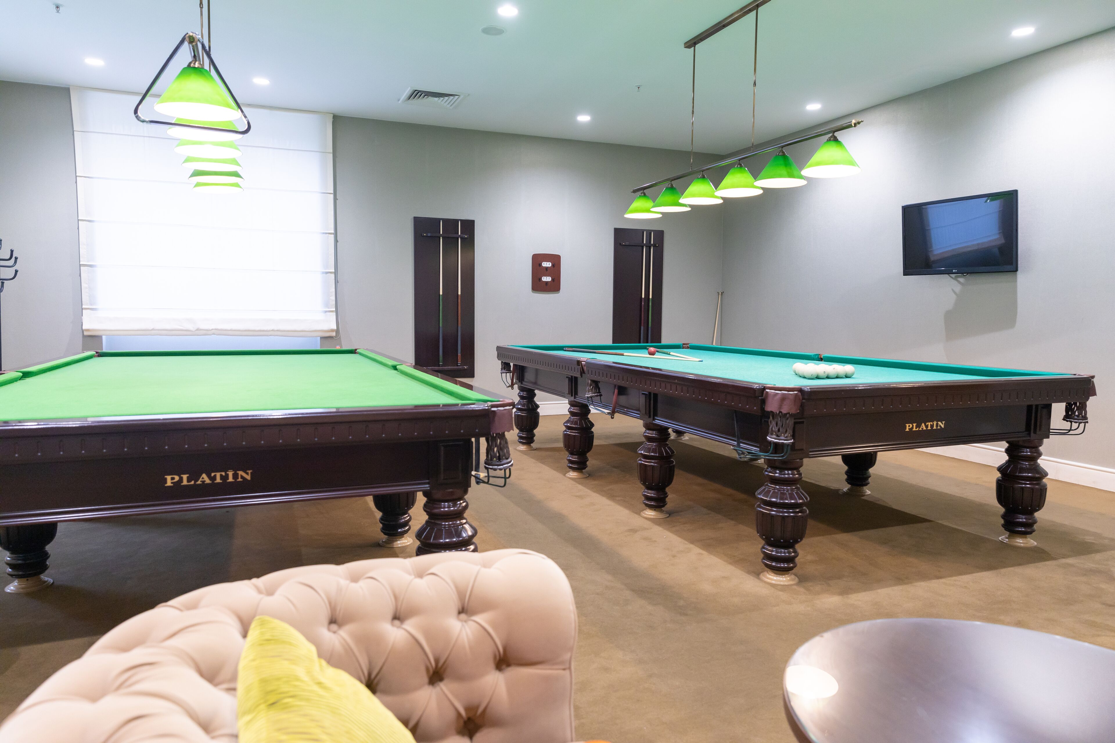Un espace dédié aux jeux de billard, comprenant deux tables de billard, un fauteuil à capitons et un téléviseur fixé au mur.