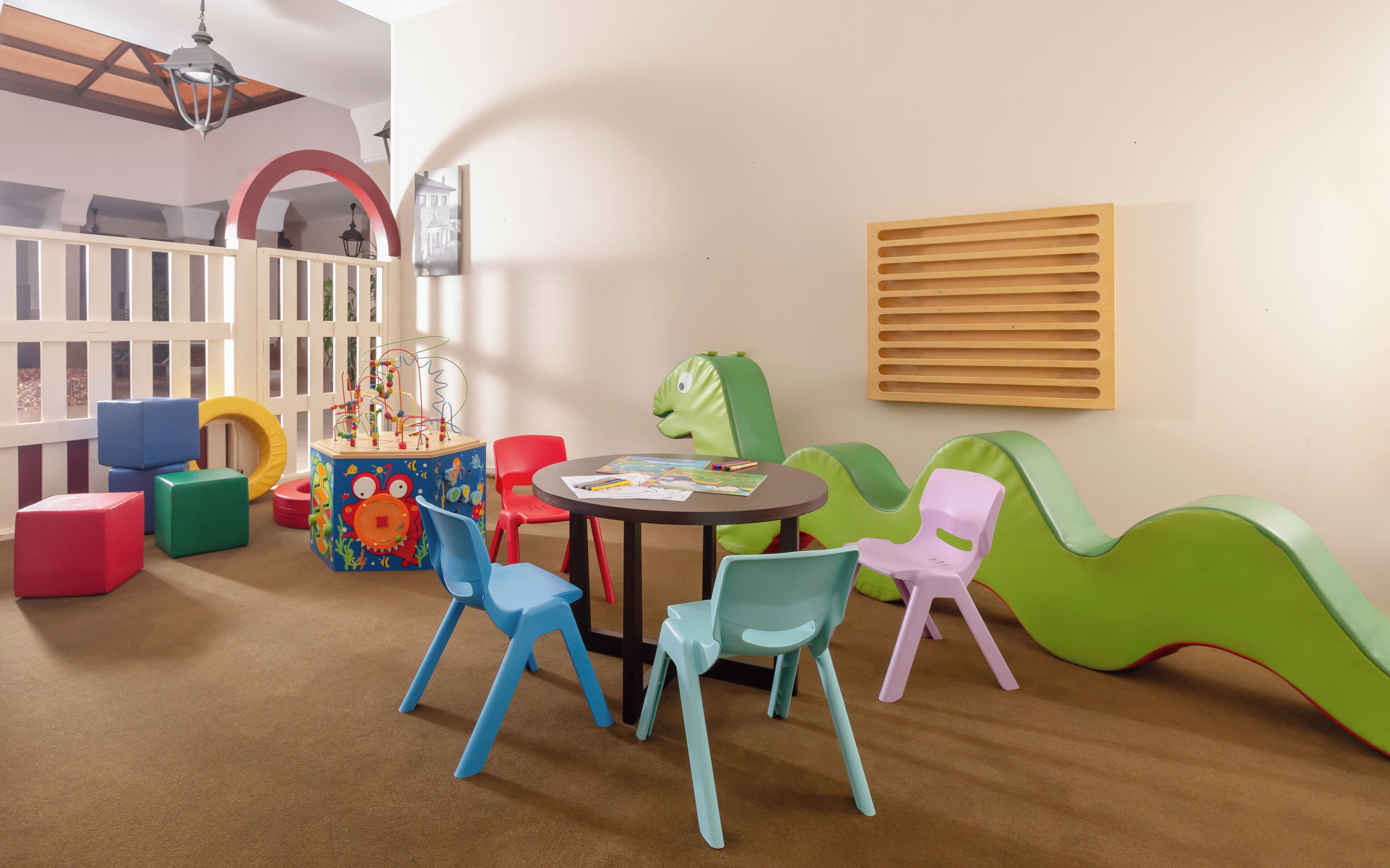Un espace de jeux pour enfants avec des chaises colorées, une table à jeux et un mur décoratif.