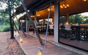 An outdoor dining area with wooden flooring, tables, chairs, and hanging lights. - Simbavati Trails Camp (Bushbuckridge)