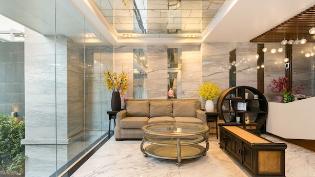 A modern lobby with a glass wall, a round glass coffee table, a sofa, and a wooden side table with a vase of flowers. - OYO 864 Hoang Anh Anh (Ho Chi Minh City)