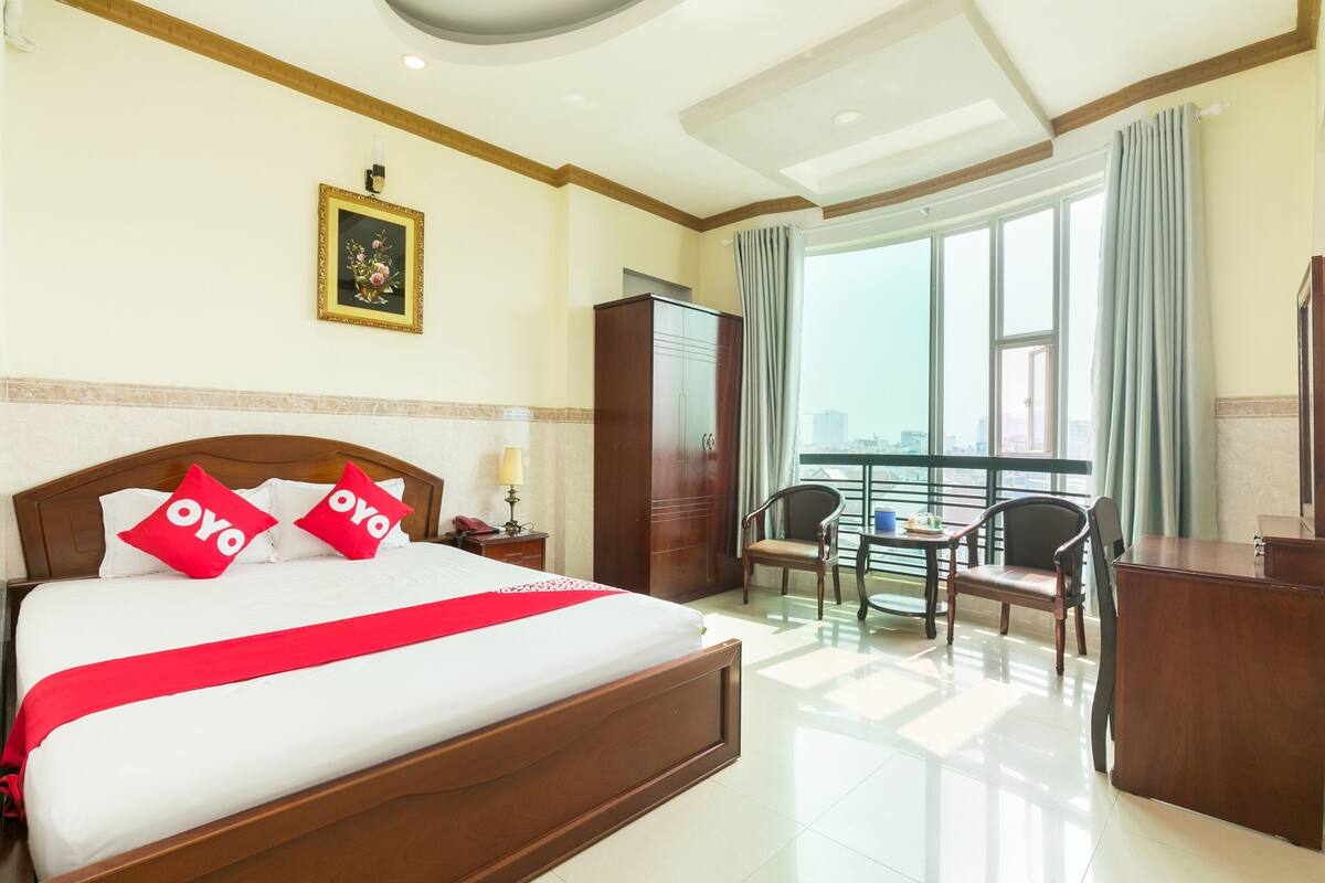 A hotel room with a large bed, a desk, a chair, a wardrobe, and a balcony with a view.