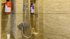 Un área de ducha con un cabezal de ducha de mano y un grifo instalado en la pared. Hay dos repisas con botellas de champú y acondicionador.