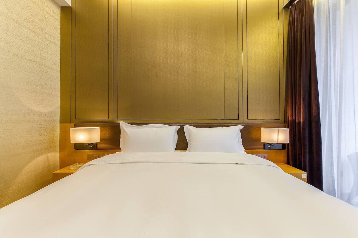 Een hotelkamer met een groot bed, twee bedlampen en een hoofdeinde met een houten paneelmotief.