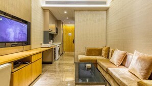 Un espacio habitable funcional con sofá, una mesita de centro, televisor, área de cocina con microondas y lavadora.