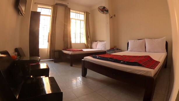 Hotelkamer met twee bedden, een bureau, een stoel, een televisie en een raam met gordijnen.