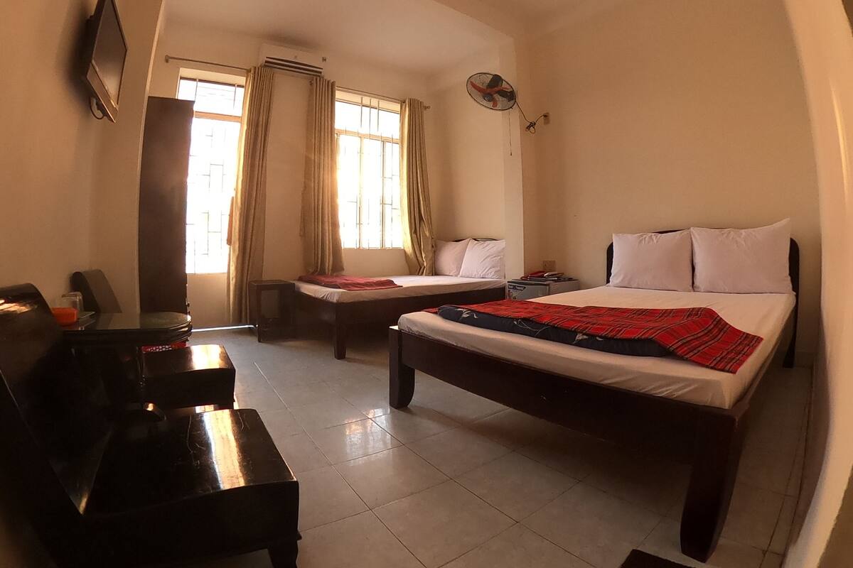 A hotel room with two beds, a desk, a chair, a TV, and a window with curtains.