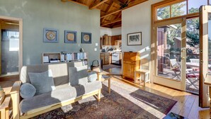 A spacious living room with a high ceiling, a sofa, a coffee table, and a rug. There is a kitchen in the background and a sliding glass door leading to an outdoor patio area. - Romantic Ridgetop Escape w/ Hot Tub Near Mendocino (Albion)