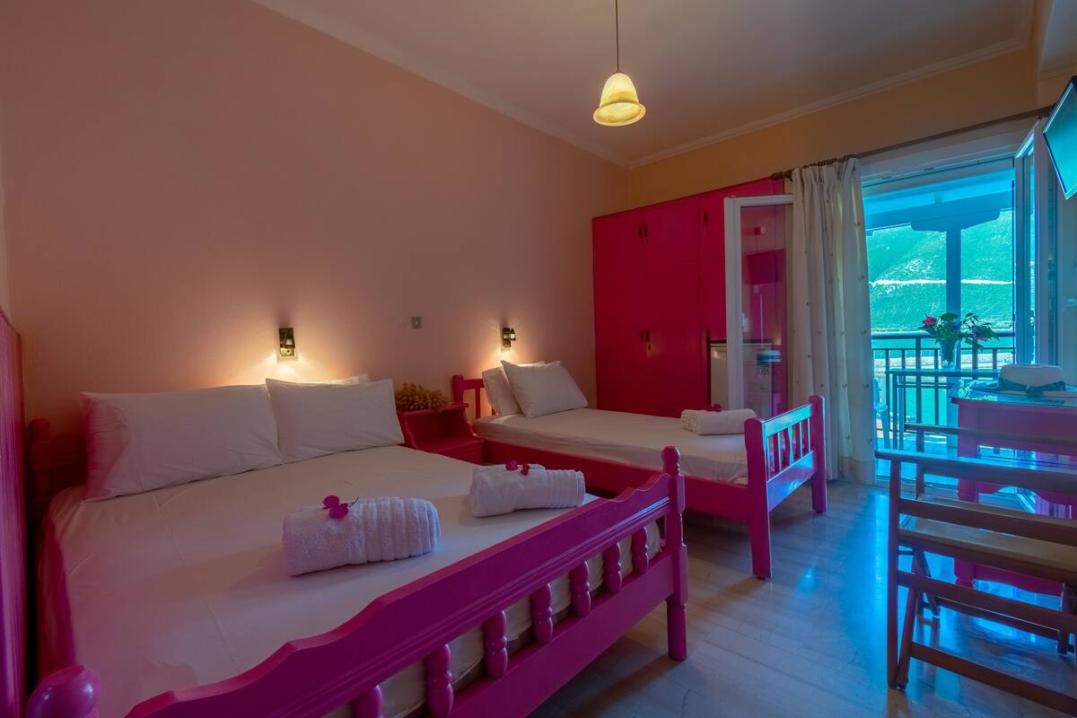 A hotel room with two beds, a balcony with a table and chairs, and a view of the outdoors.