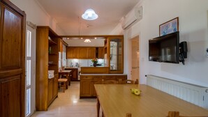 Eine geräumige Küche mit Holzausstattung, einem Esstisch und Stühlen. Ein Fernseher ist an der Wand angebracht und ein Fenster lässt Tageslicht herein.